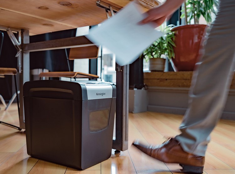 A man is inserting a paper sheet into a Kensington shredder.