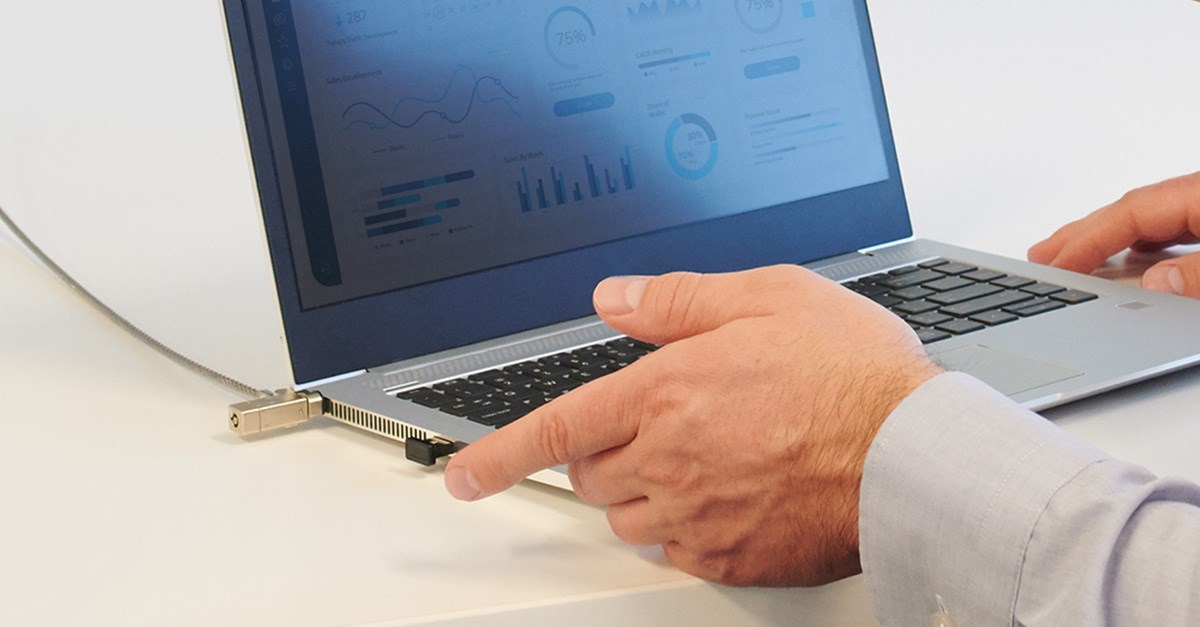 Laptop locked with a Kensington lock showing analytics on screen, with hands interacting.