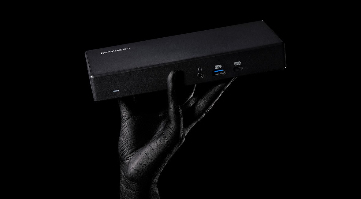 A dark image featuring a Kensington SD4782P EQ USB-C & USB-A Dual 4K Docking Station held in a human hand. 