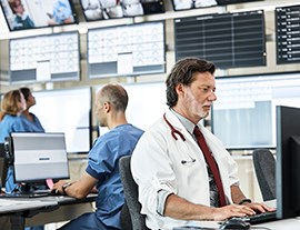 Male doctor working with his computer and surrounded by other doctors.