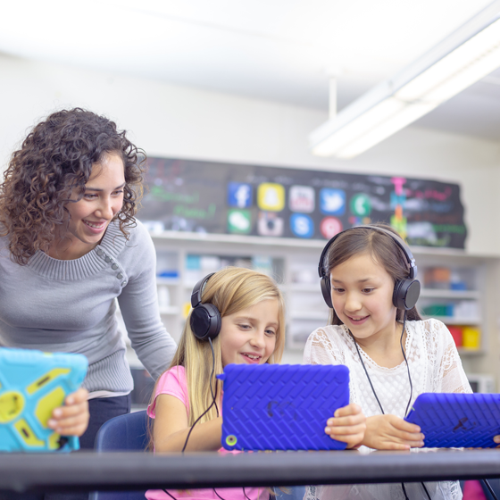 a teacher assisting 2 children using tablets.