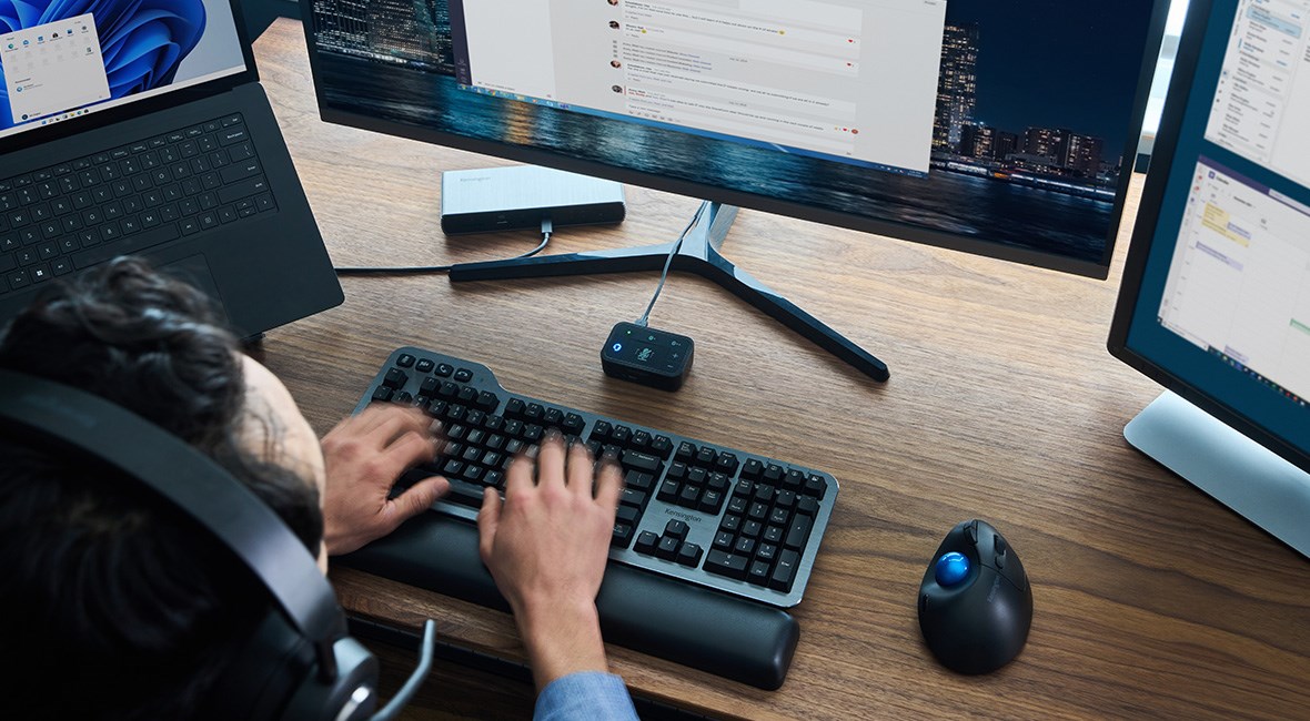 Over shoulder view of man working at desk while wearing H3000 headphones, typing on silent mechanical keyboard with wrist rest