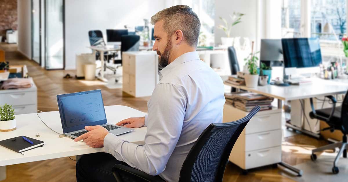 Man sitting at a desk in an open office with a Kensington lock securing his laptop