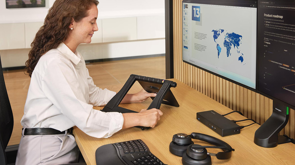 Woman sitting at an office desk adjusting a Kensington laptop cooling stand