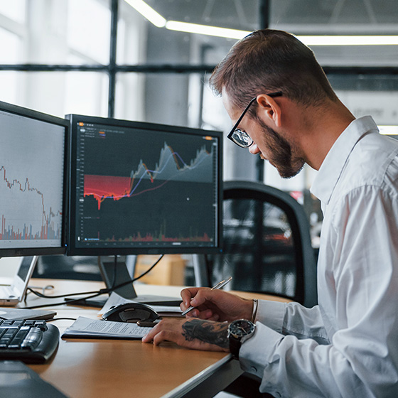 Male working in office environment with dual monitors featuring graphs.